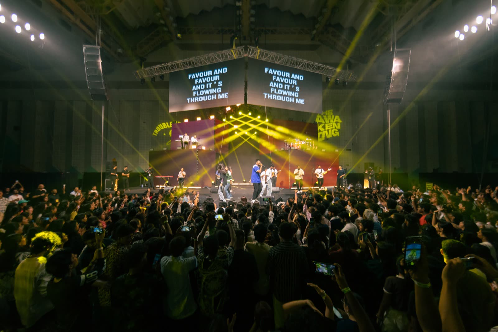 A packed arena worshipping toward a brightly lit stage with lyrics on the screens