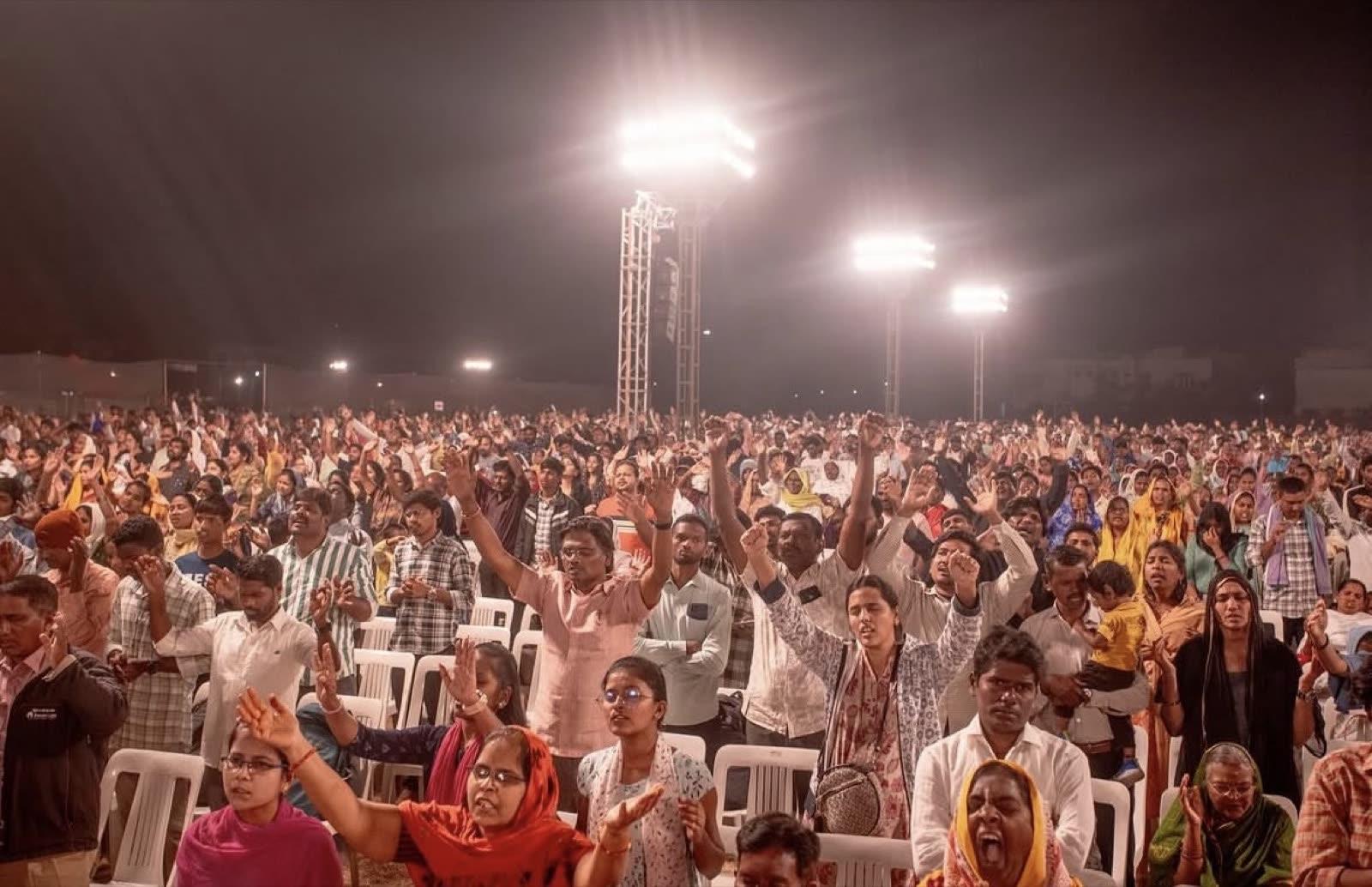 Close view of a night crowd with many hands raised in worship and prayer